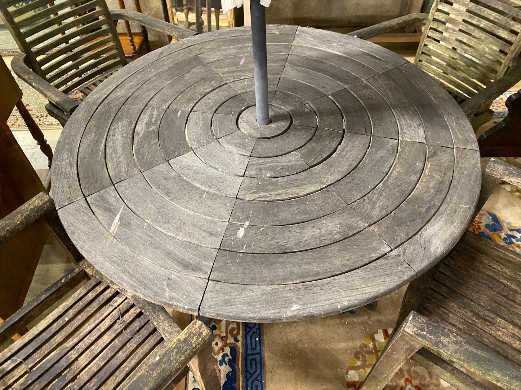 A circular weathered teak garden table, diameter 130cm, height 71cm together with four elbow chairs and a crank parasol